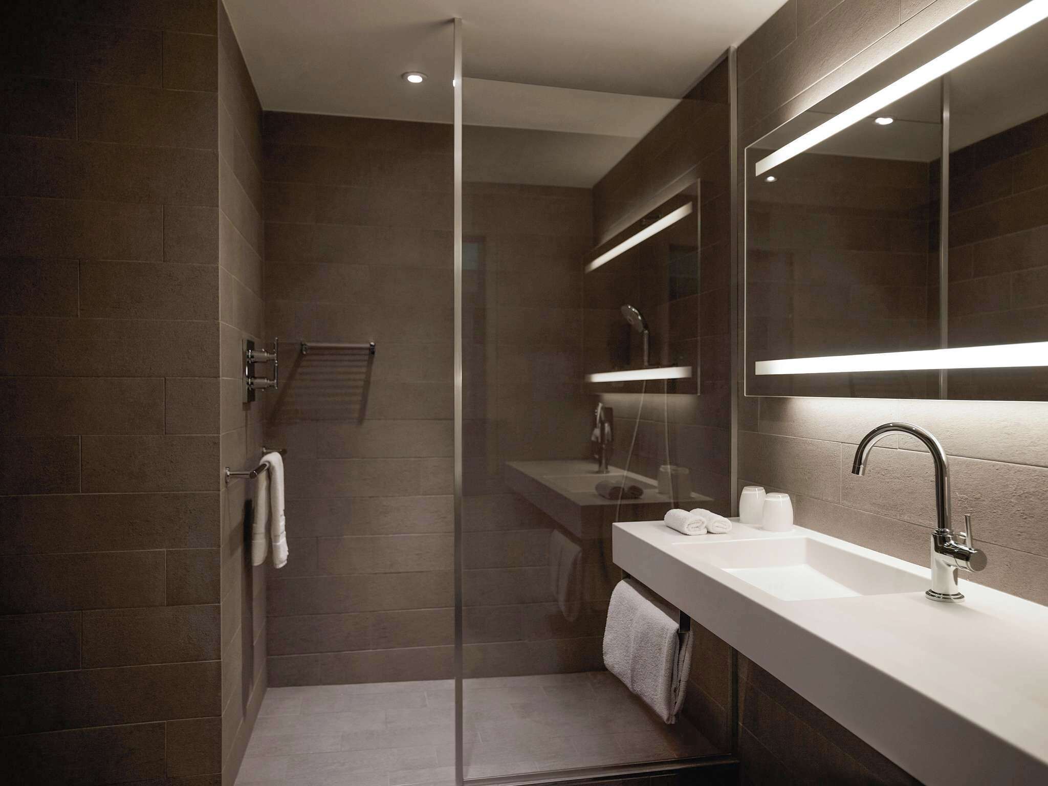 A modern bathroom with a glass shower enclosure, a white sink with a chrome faucet, and a large mirror above the sink.