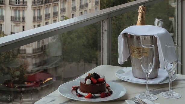 Un tavolo con dessert e bicchieri da champagne, una bottiglia di champagne e vista sulla Torre Eiffel sullo sfondo.