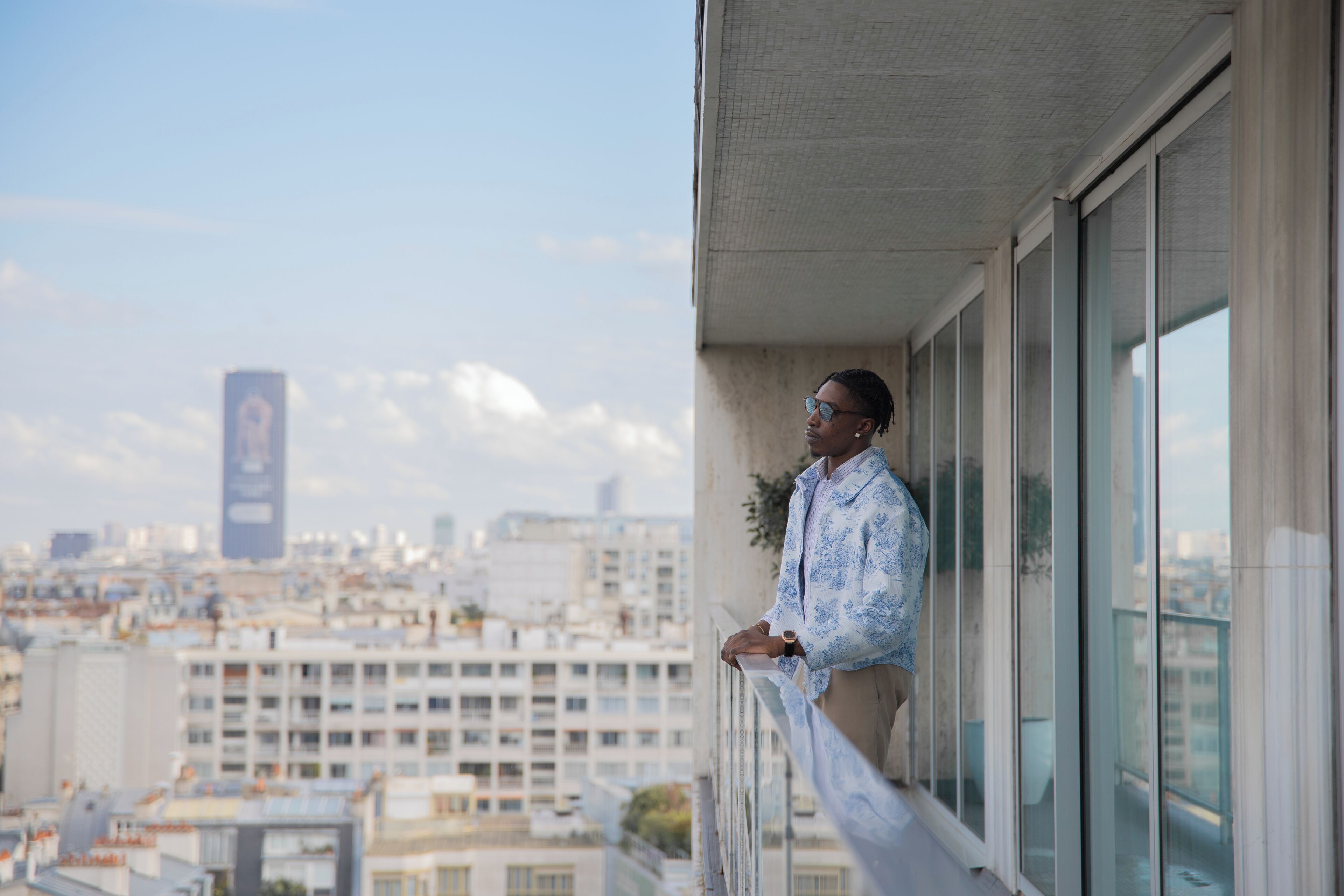 Une personne se tient sur un balcon, avec une vue sur le paysage urbain.