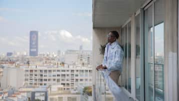 Une personne se tient sur un balcon, avec une vue sur le paysage urbain.
