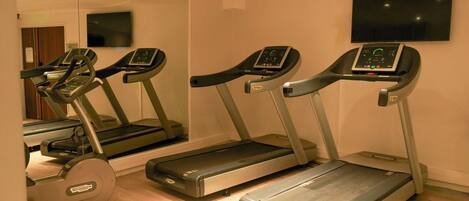 Tres cintas de correr en una sala con un espejo grande y un televisor en la pared.