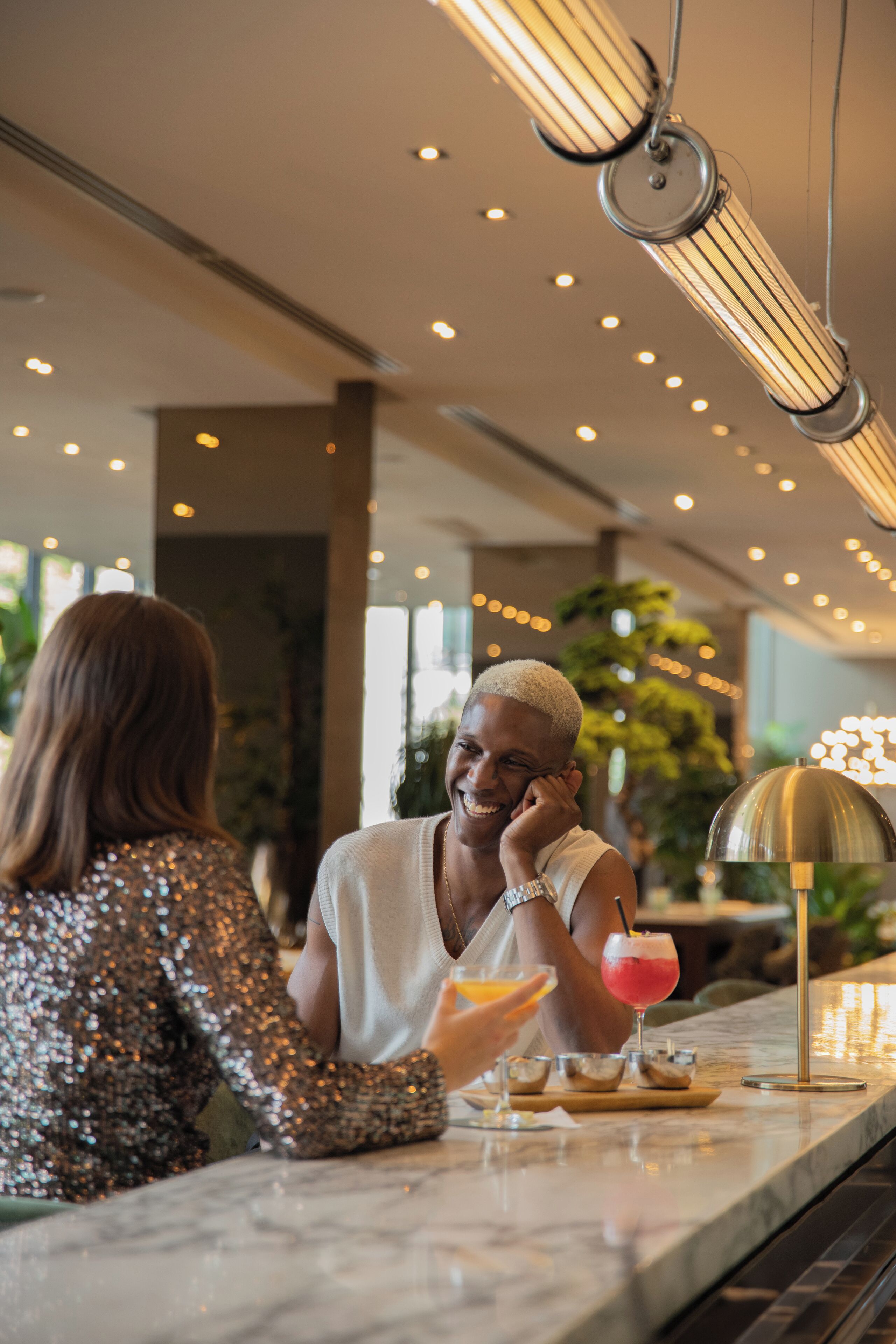 A bar area with a marble countertop, a drink with a pink straw, and a gold lamp.