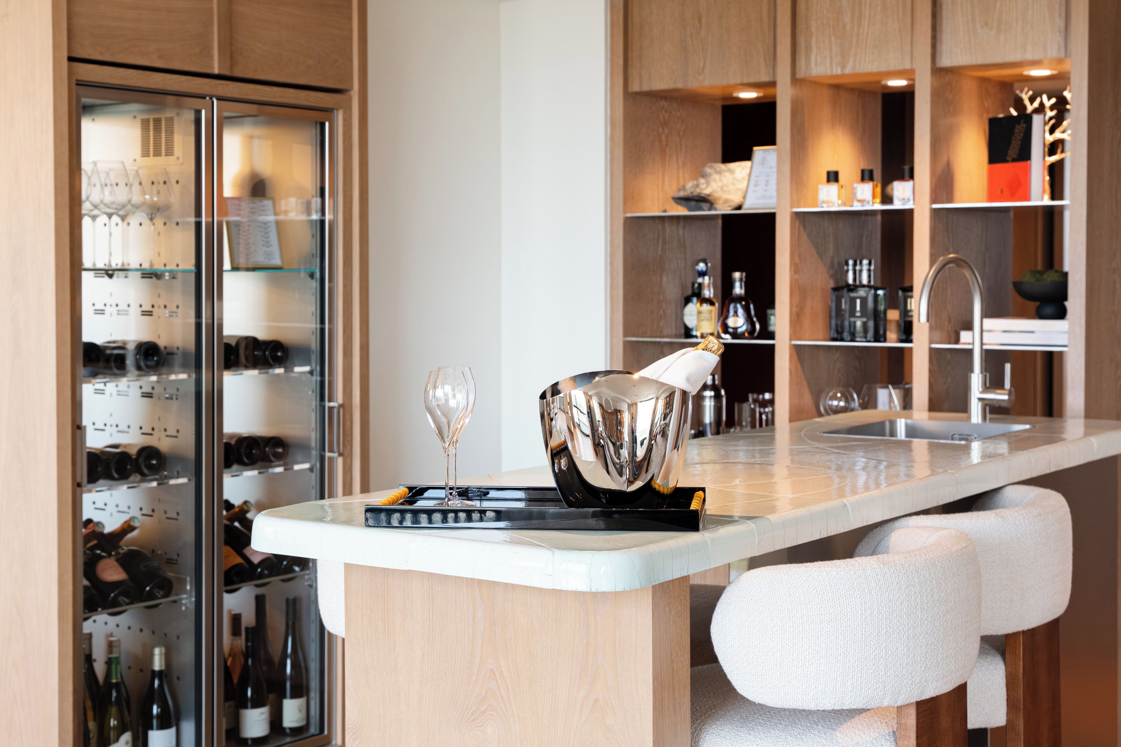 Eine moderne Küche mit Weinkühlschrank, Weinflaschen, einem Weinglas und einer Bar mit Flaschen und Spüle.