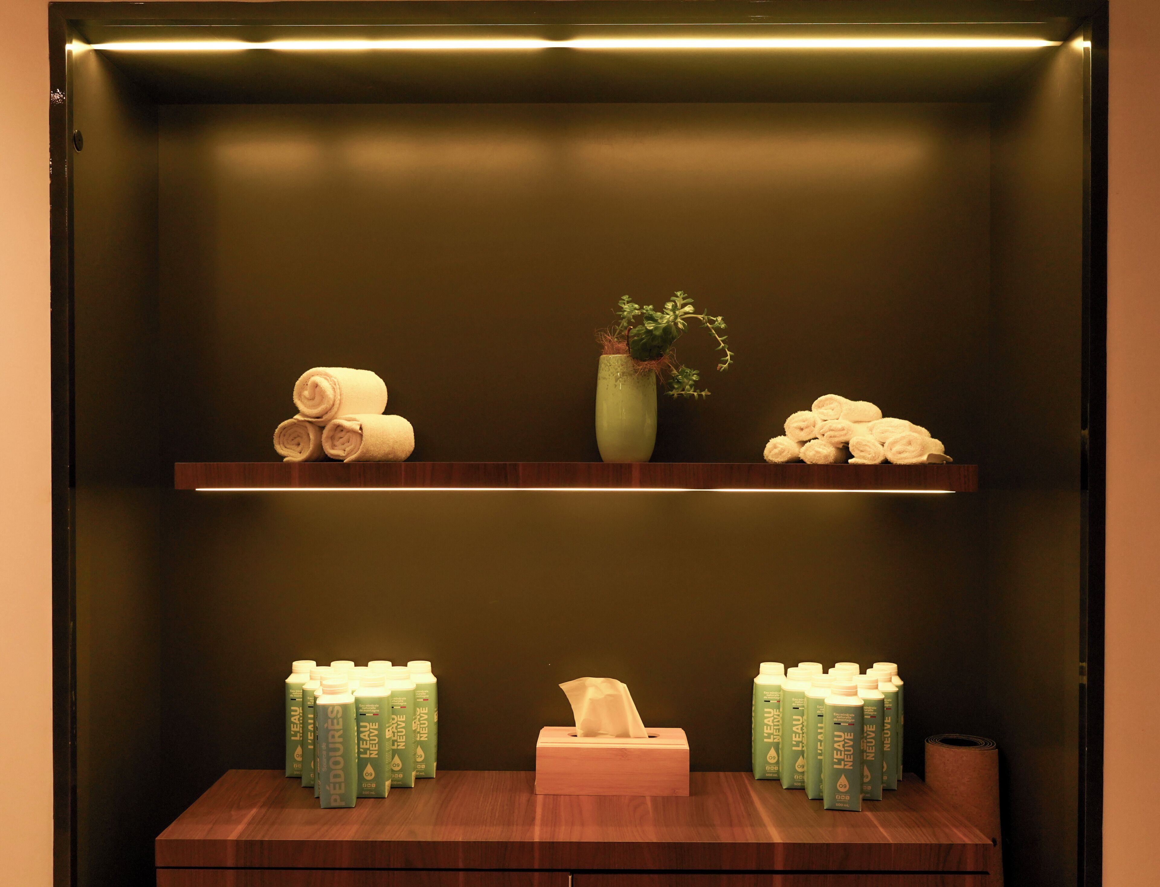 Un baño con dos estantes de madera, un florero con planta y toallas y botellas de Eau de Parfums ordenadas.