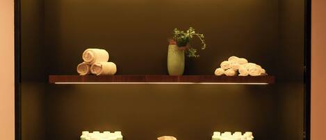 Un baño con dos estantes de madera, un florero con planta y toallas y botellas de Eau de Parfums ordenadas.