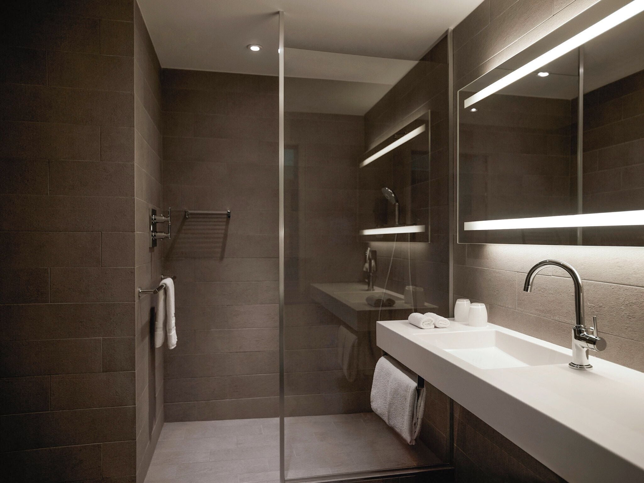 Een moderne badkamer met een douchecabine van glas, een wit wastafelmeubel met een spiegel erboven en een handdoekrek.