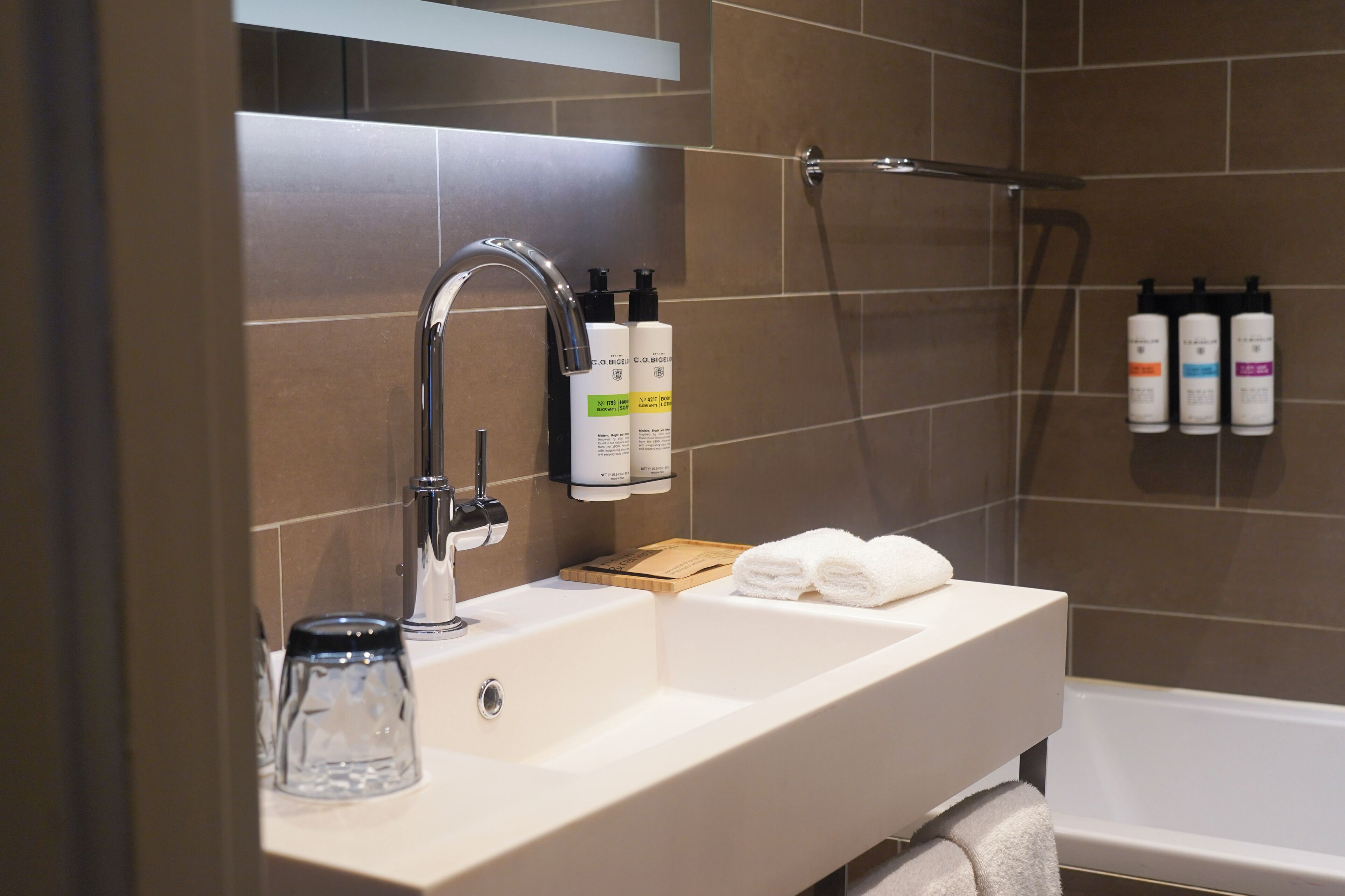 A bathroom with a white sink, a glass jar, and toiletries on the wall.