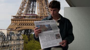 A person reading a newspaper with the Eiffel Tower in the background.