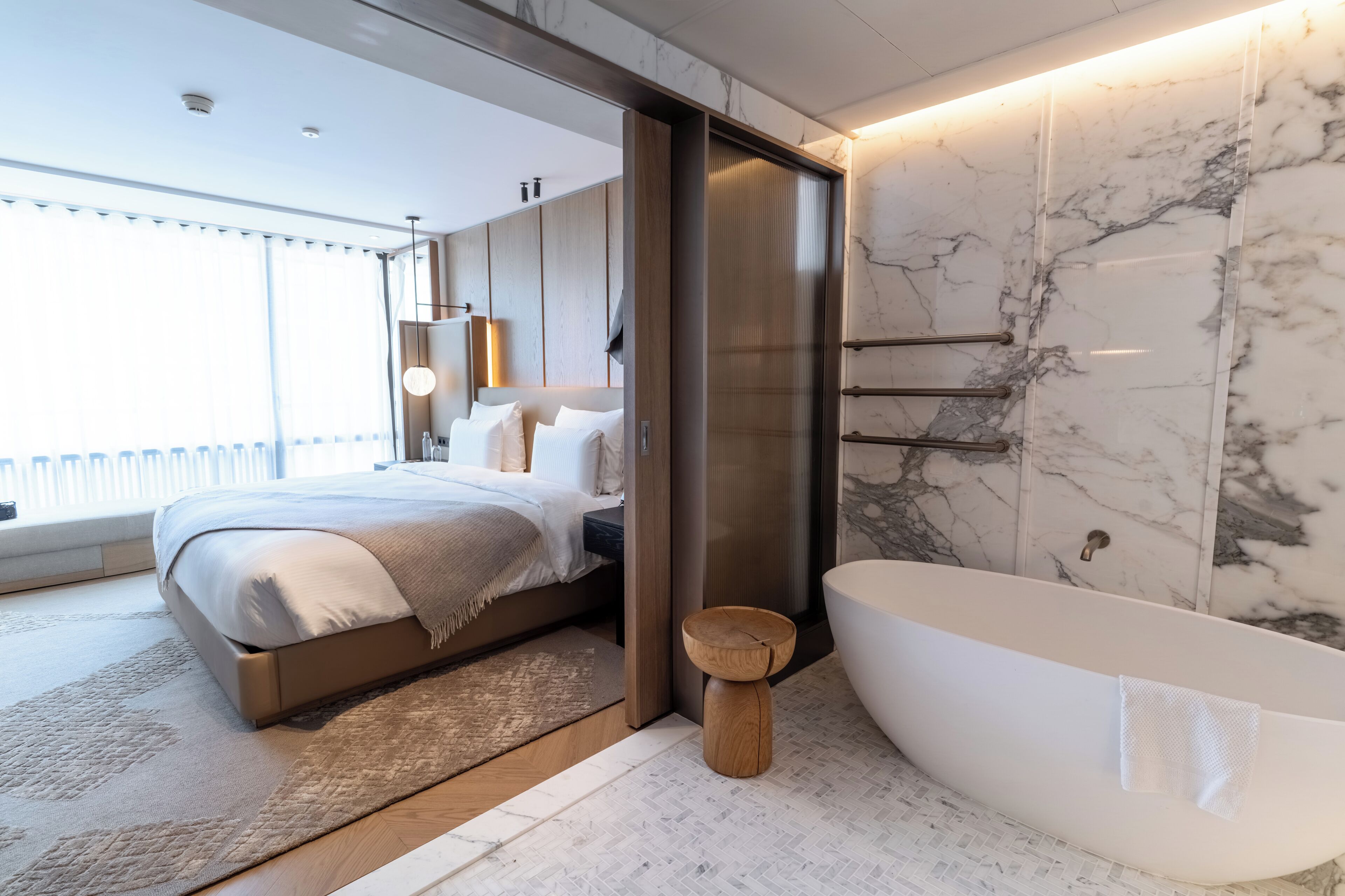Une chambre moderne avec un grand lit, un tabouret en bois et une baignoire sur pieds.