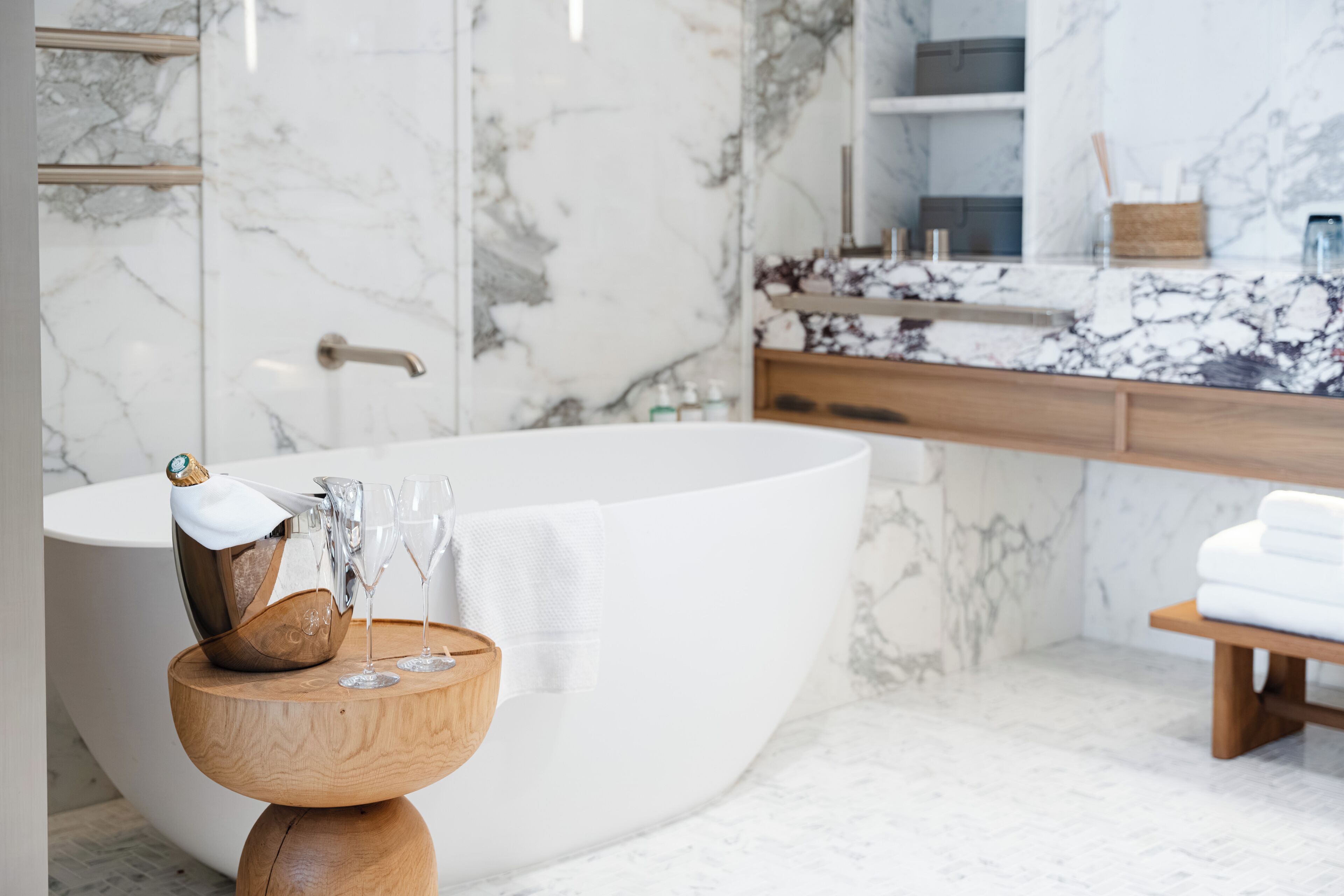 Un baño moderno con una bañera independiente, paredes de mármol y un mueble de tocador de madera con espejo.