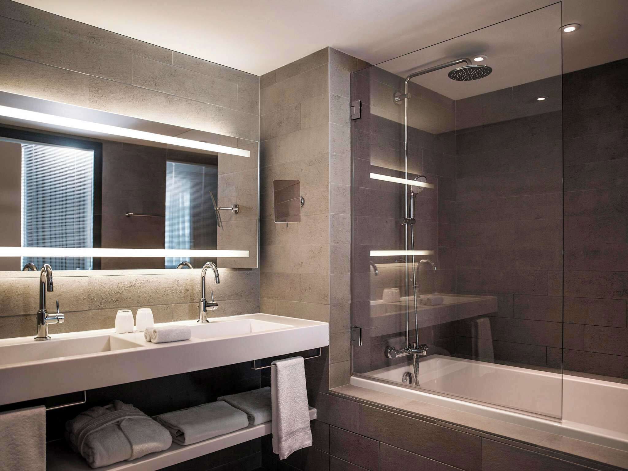 A modern bathroom with two sinks, a large mirror, a glass-enclosed shower, and a bathtub.