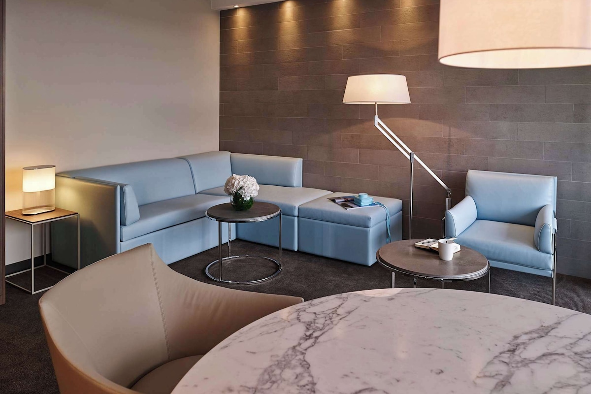 Una moderna camera d'hotel con un divano blu, un tavolino rotondo in marmo e una lampada da terra.