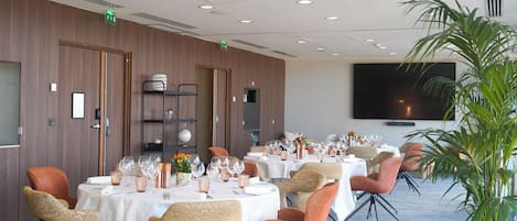 Un salón de conferencias con mesas redondas, sillas y una pantalla de televisión en la pared.