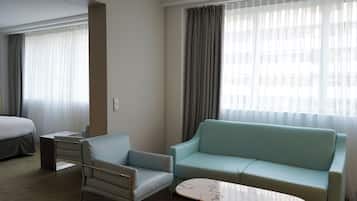 A hotel room with a bed, a light blue armchair, a light blue sofa, and a marble coffee table.
