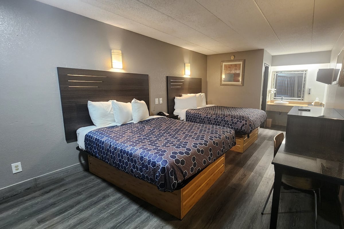 A hotel room with two beds, a desk, and a small bathroom.
