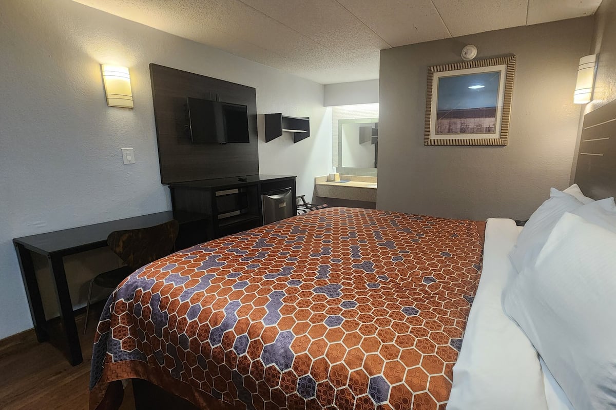 A hotel room with a large bed, a television, a desk, and a mirror.