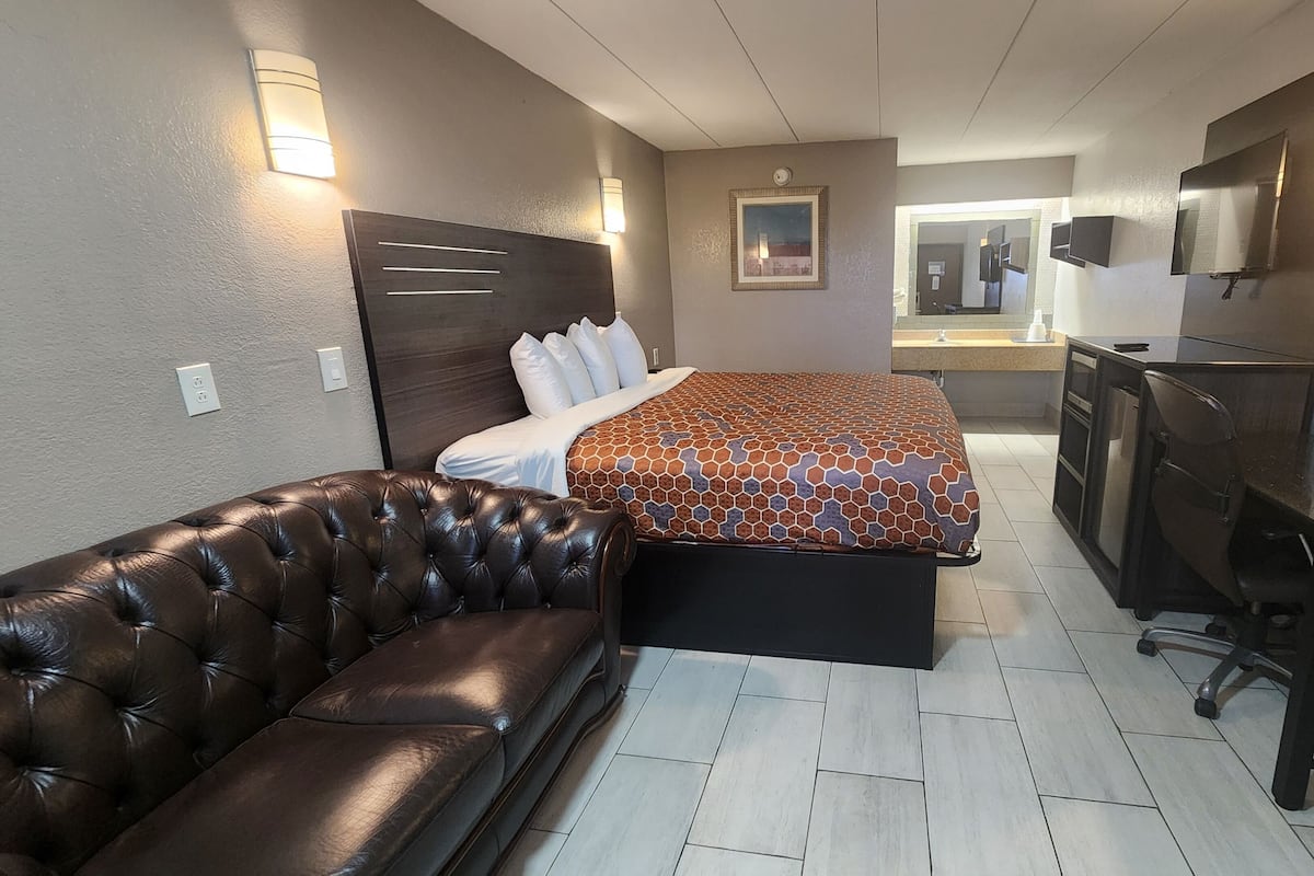A compact hotel room with a bed, a leather sofa, a desk, and a television.