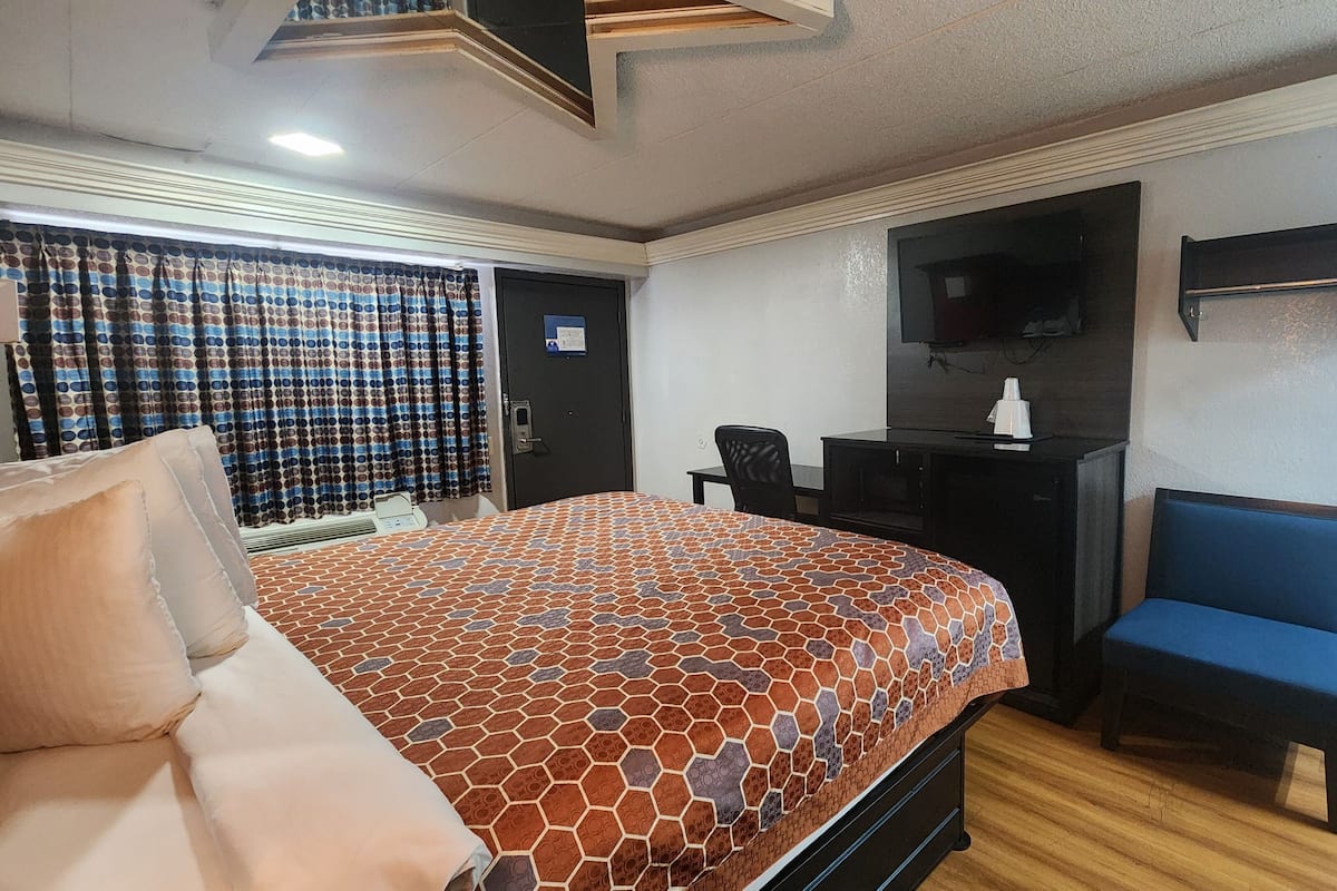 A hotel room with a bed, a desk, a chair, a TV, and a curtain.