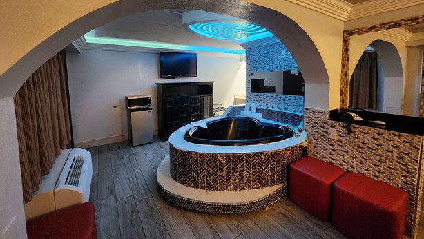 Un intérieur moderne avec un espace salon circulaire central, un téléviseur à écran plat, un réfrigérateur et un mur décoré de motifs.