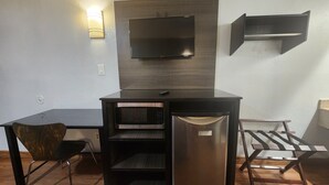 Une petite cuisine équipée comprenant un four à micro-ondes, un petit réfrigérateur, un téléviseur à écran plat fixé au mur et une chaise.