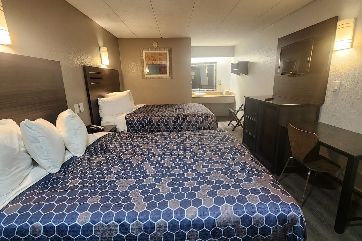 A hotel room with two beds, a desk, a chair, a dresser, and a mirror.