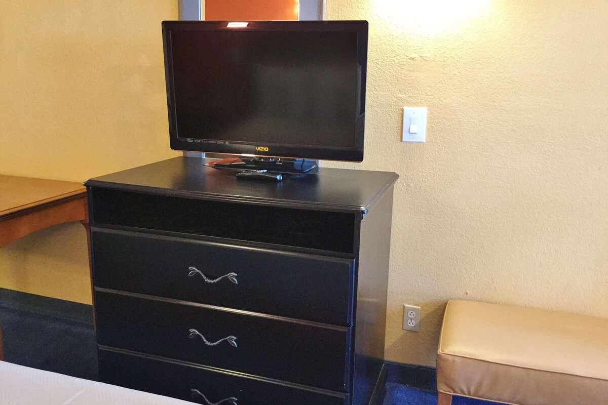 A black TV on a dresser with drawers, a power outlet, and a wall socket.