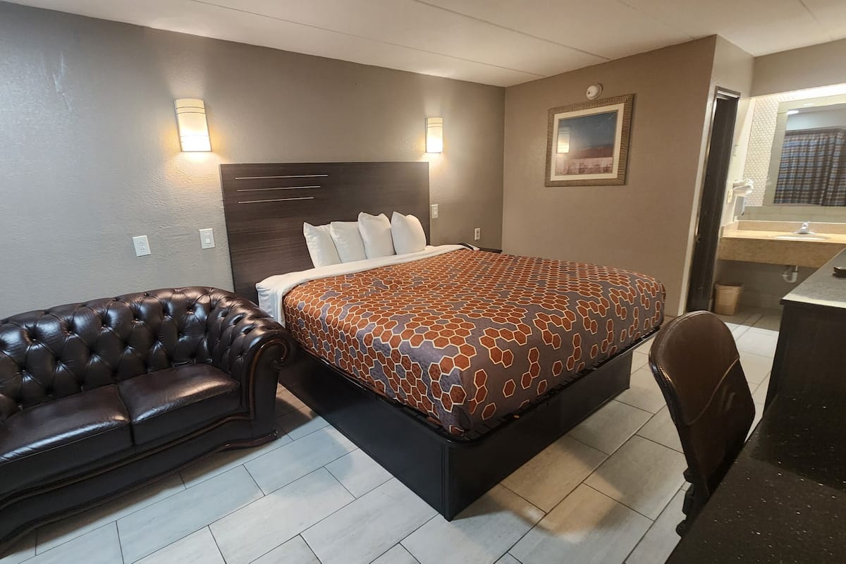 A hotel room with a large bed, a leather sofa, a desk with a mirror, and two wall-mounted lights.
