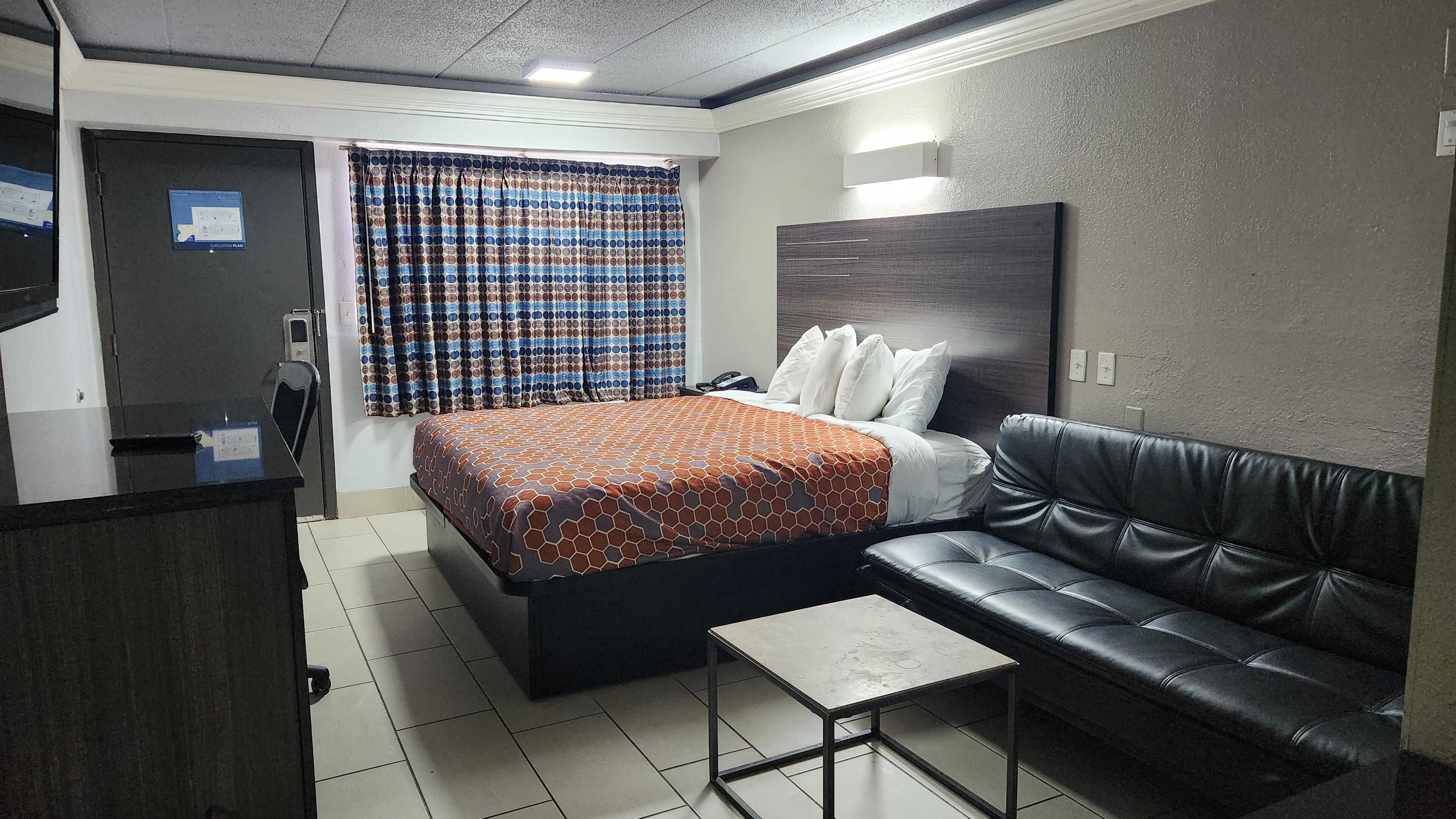 A hotel room with a bed, a black leather sofa, a small table, and a curtain with a polka dot pattern.