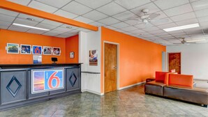 A motel lobby with a reception desk, a large number '6' sign, a seating area, and a door. - Motel 6 Calhoun, GA (Calhoun)