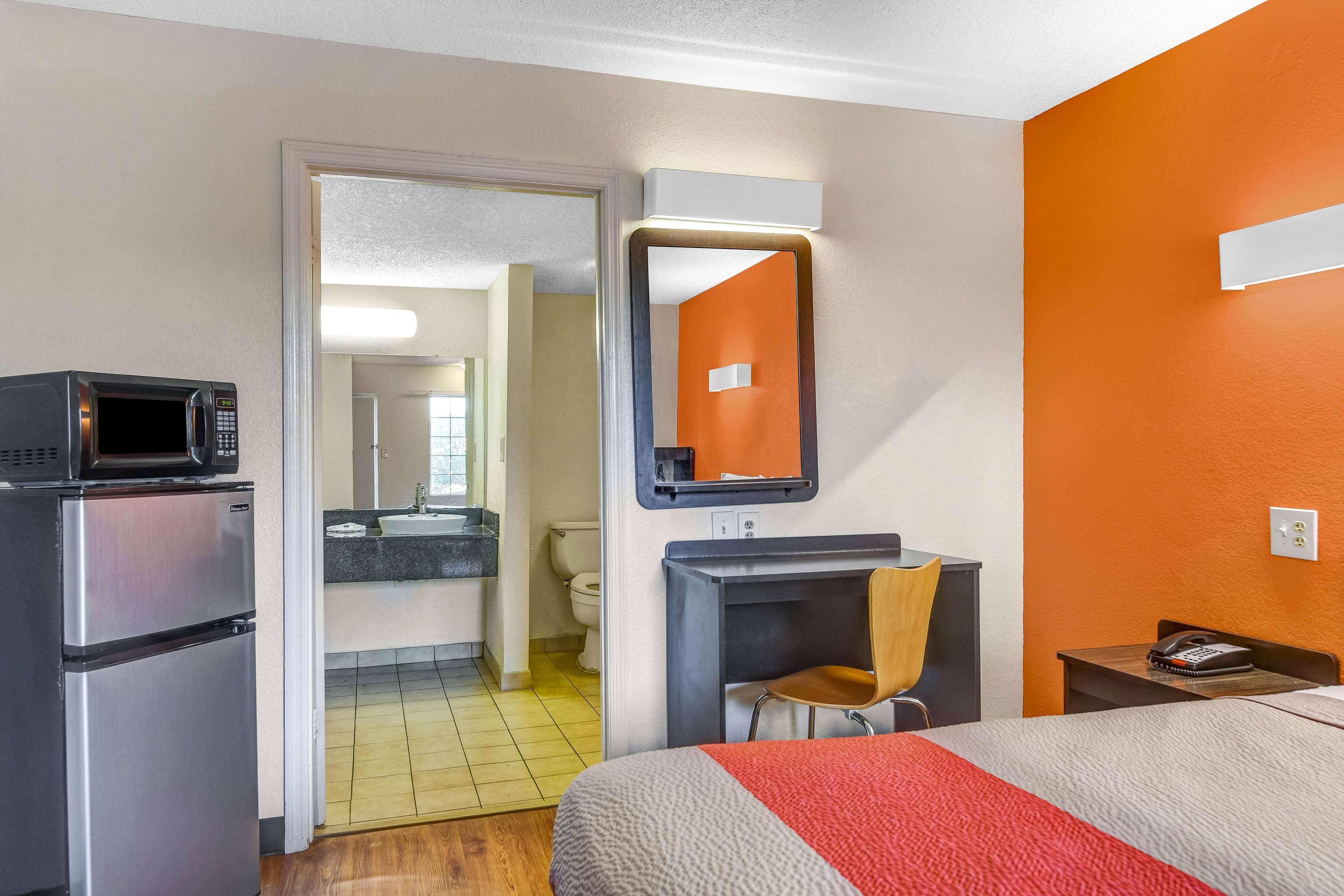A hotel room with a bed, a microwave, a desk, a chair, and a bathroom visible through an open door.