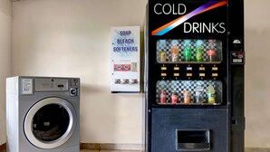 A laundry area with a washing machine and a vending machine offering cold drinks and soap, bleach, and softeners. - Motel 6 Calhoun, GA (Calhoun)