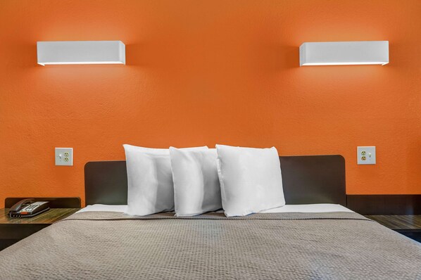 A hotel room with an orange wall, a bed with white pillows, and a nightstand with a phone.