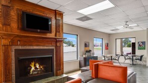 A modern lobby with a fireplace, comfortable seating, a television, and large windows offering views of the outside. - Motel 6 Calhoun, GA (Calhoun)