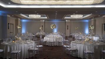 A banquet hall with round tables, clear chairs, and chandeliers.