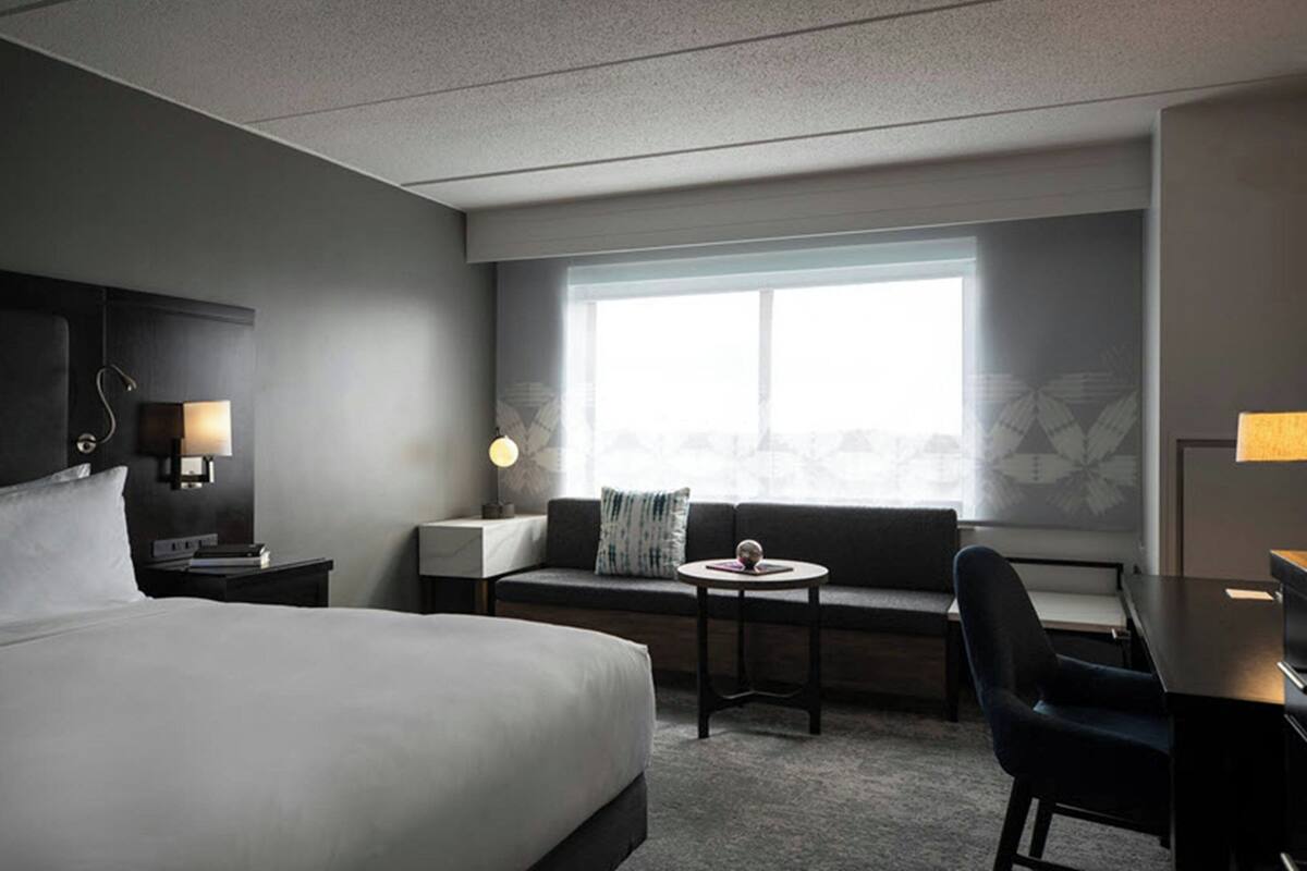 A hotel room with a large bed, a desk, a chair, a small table, and a window with a view.