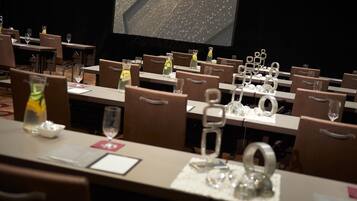 Un salón de conferencias con mesas dispuestas para una reunión, equipado con tarjetas de identificación, botellas de agua y vasos.