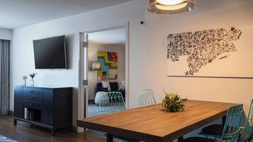 A modern dining area with a wooden table and teal chairs, a flat-screen TV on the wall, and a cityscape artwork.