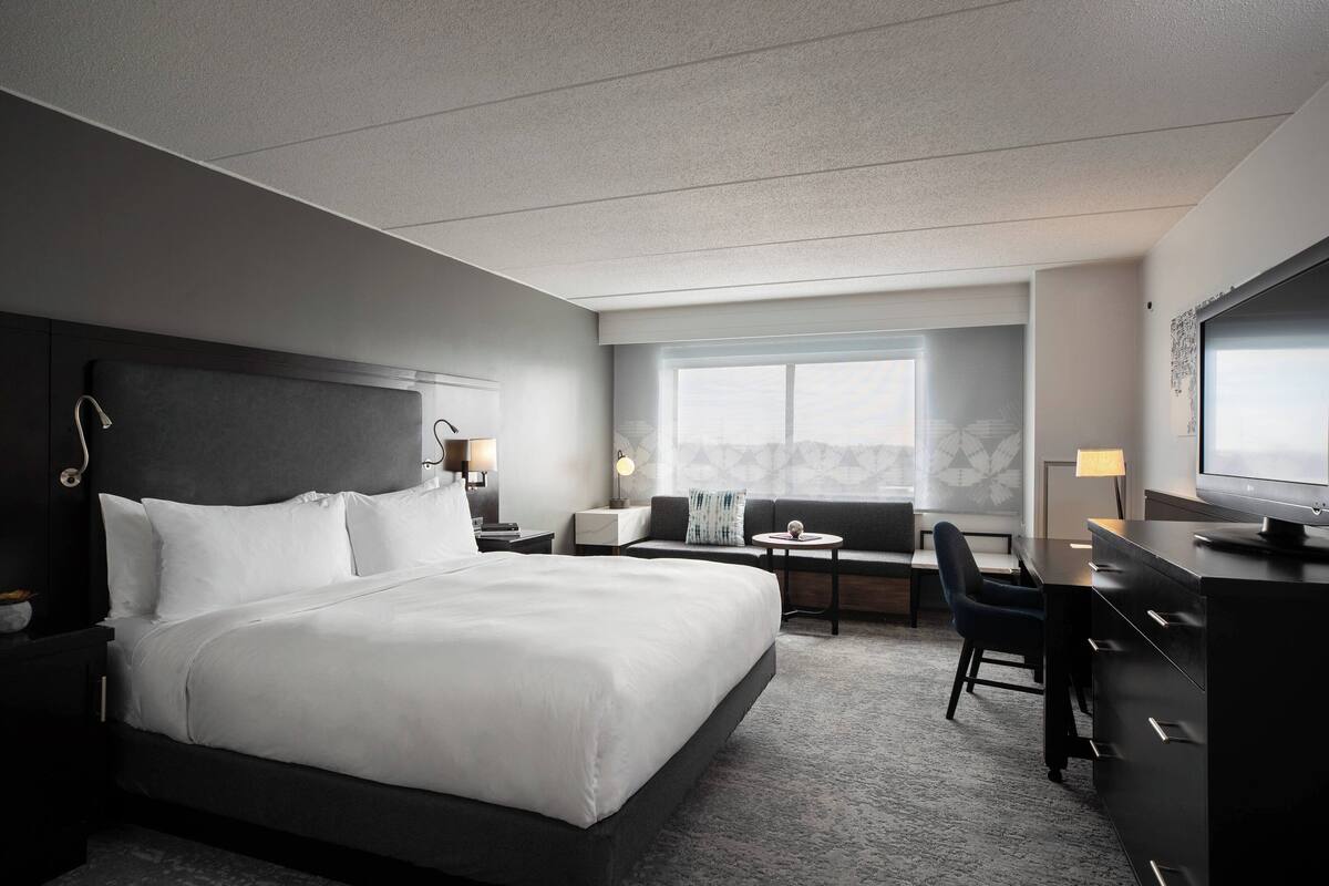 A modern hotel room with a large bed, a desk, a chair, and a TV.