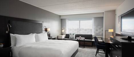 A modern hotel room with a large bed, a desk, a chair, and a TV.