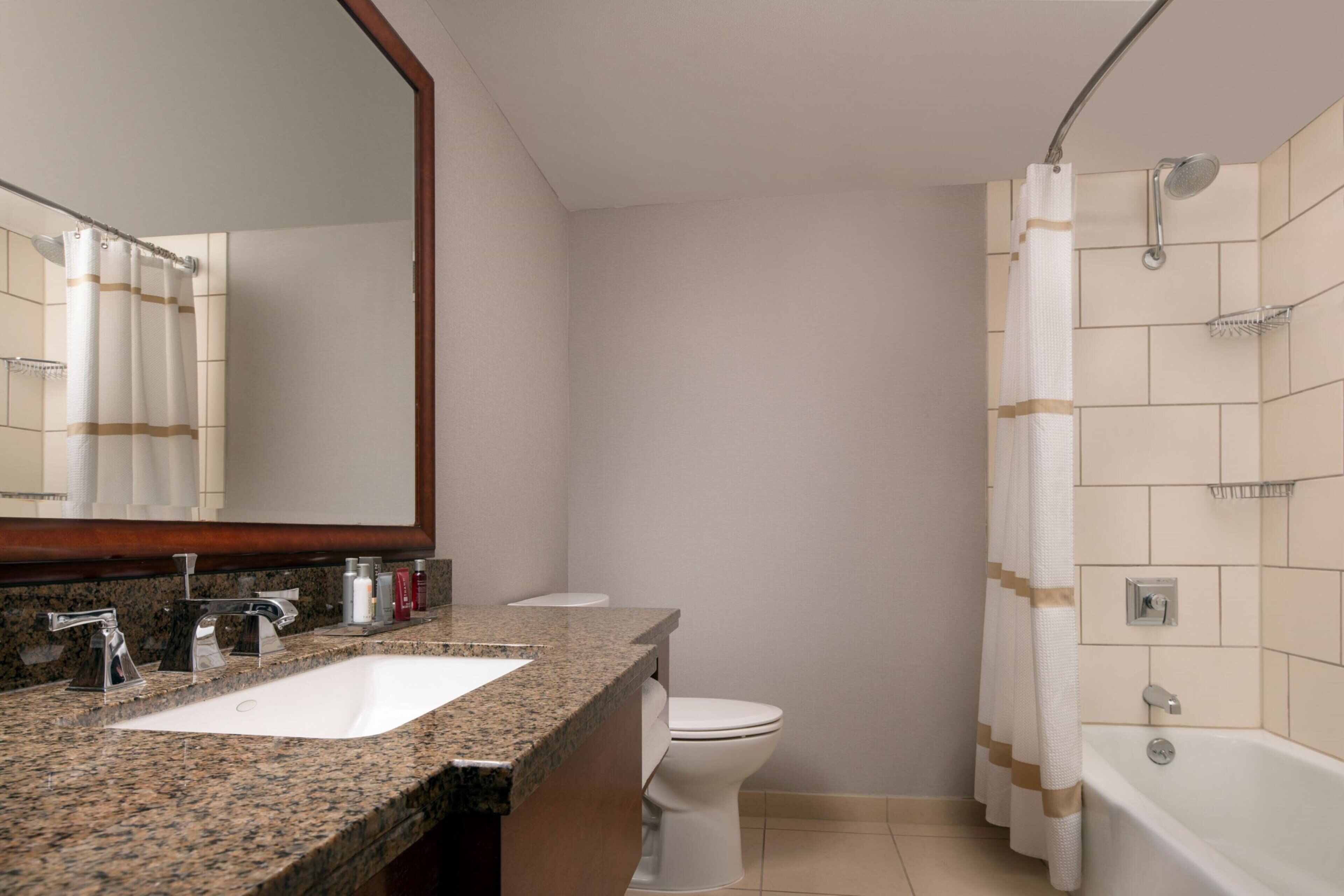 A bathroom with a granite countertop, a white sink, a toilet, and a bathtub.