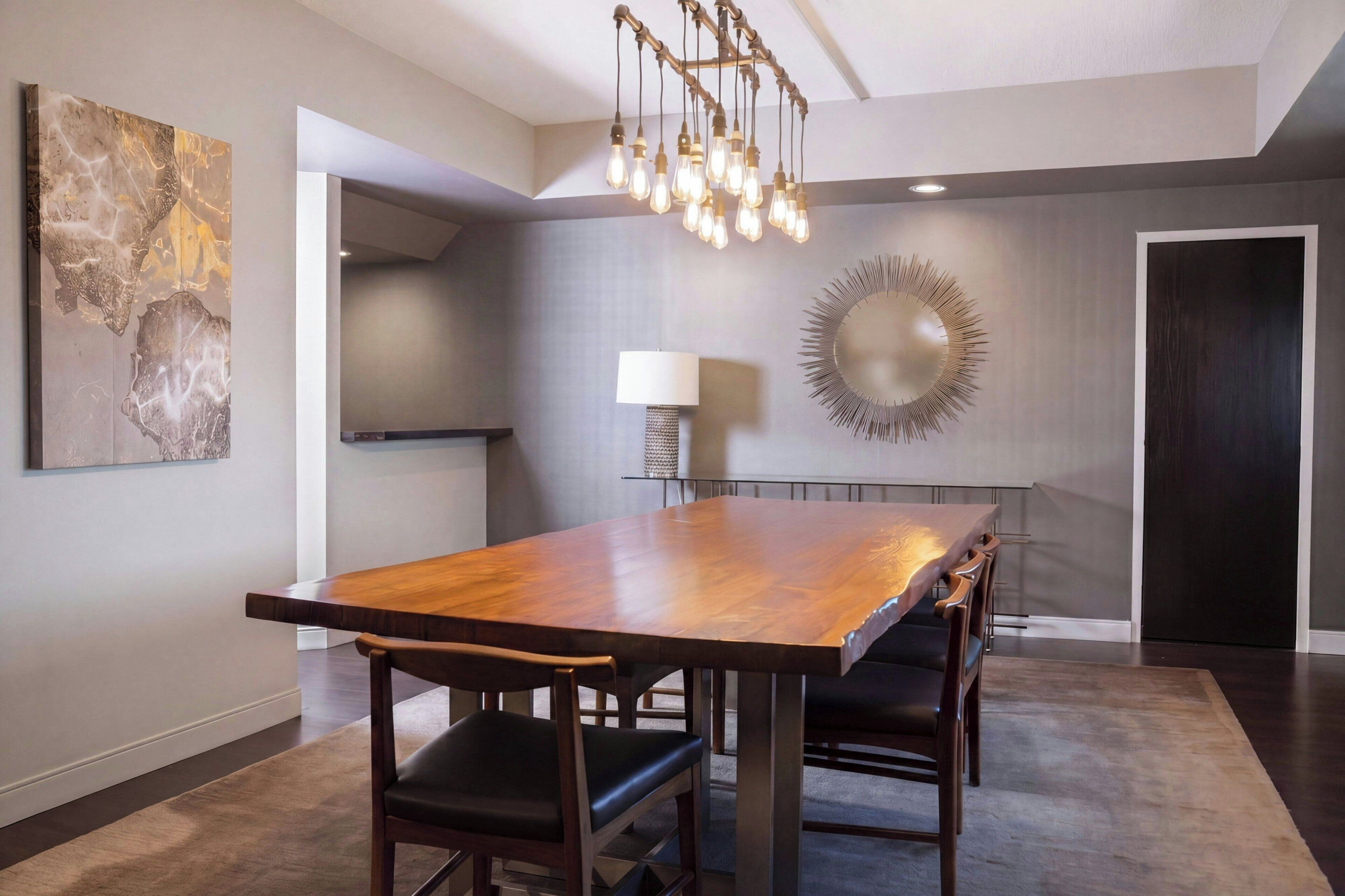 A modern dining area with a wooden table, chairs, a chandelier, and a wall-mounted lamp.