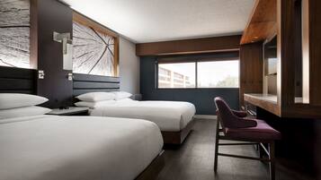 Habitación de hotel con dos camas, un escritorio, una silla, un ventanal y vistas a edificios.