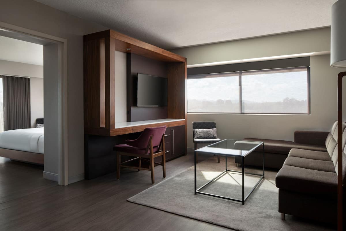 Ein modernes Hotelzimmer mit einem Bett, einem Schreibtisch mit Flachbildfernseher, einer Couch und einem großen Fenster mit Blick auf die Stadt.