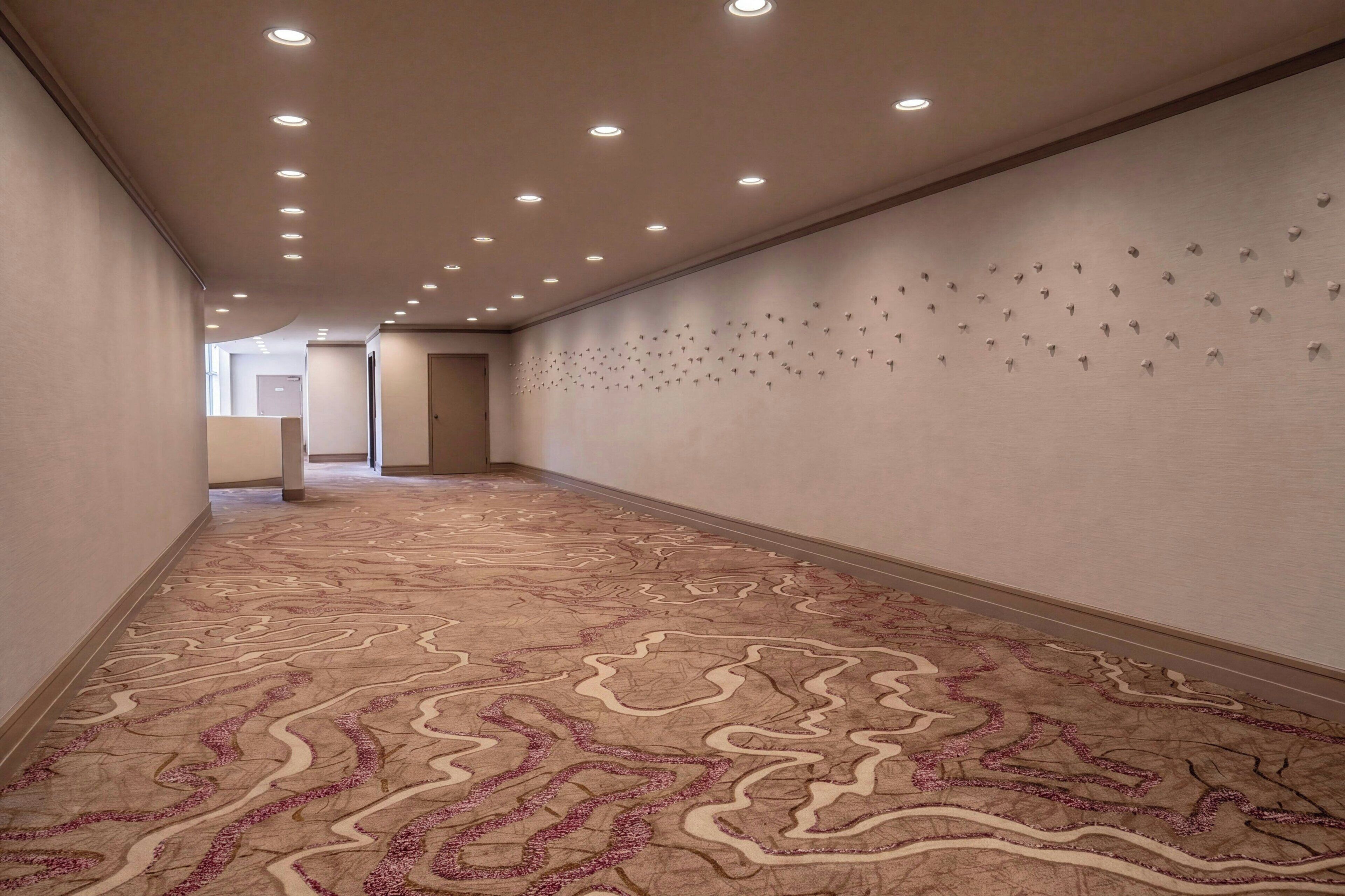 Un pasillo con alfombra estampada, luces empotradas en el techo y una pared con detalles decorativos.