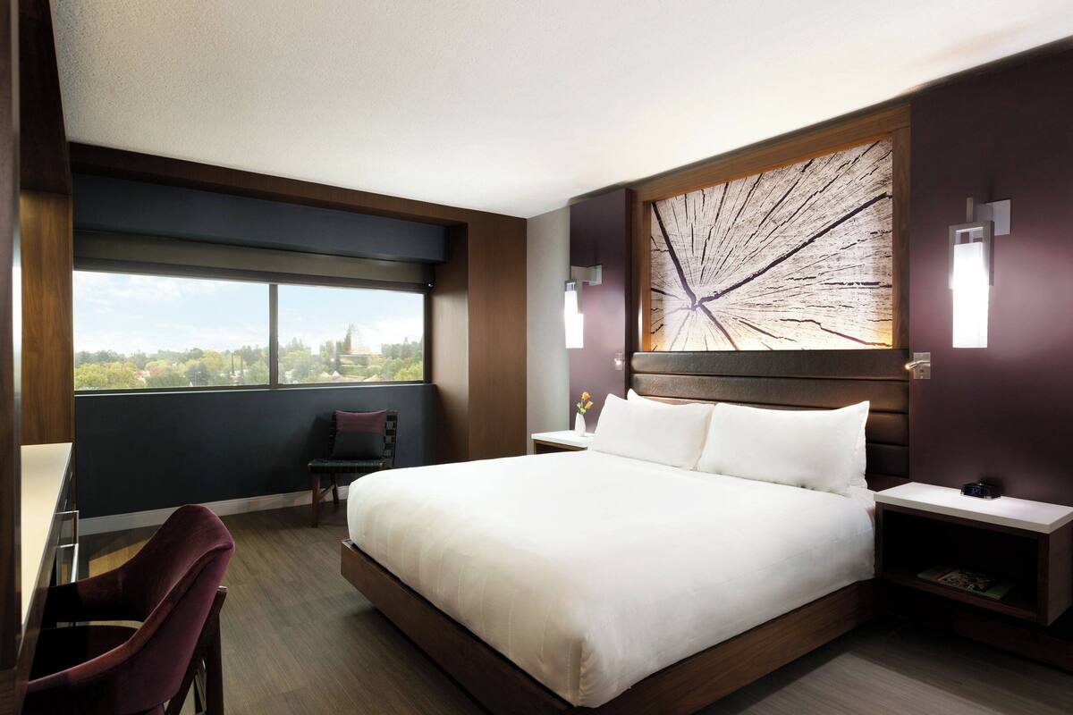 Ein Hotelzimmer mit einem großen Bett, einem Schreibtisch, einem Sessel, einem Fenster mit Aussicht und einem Wandbild.