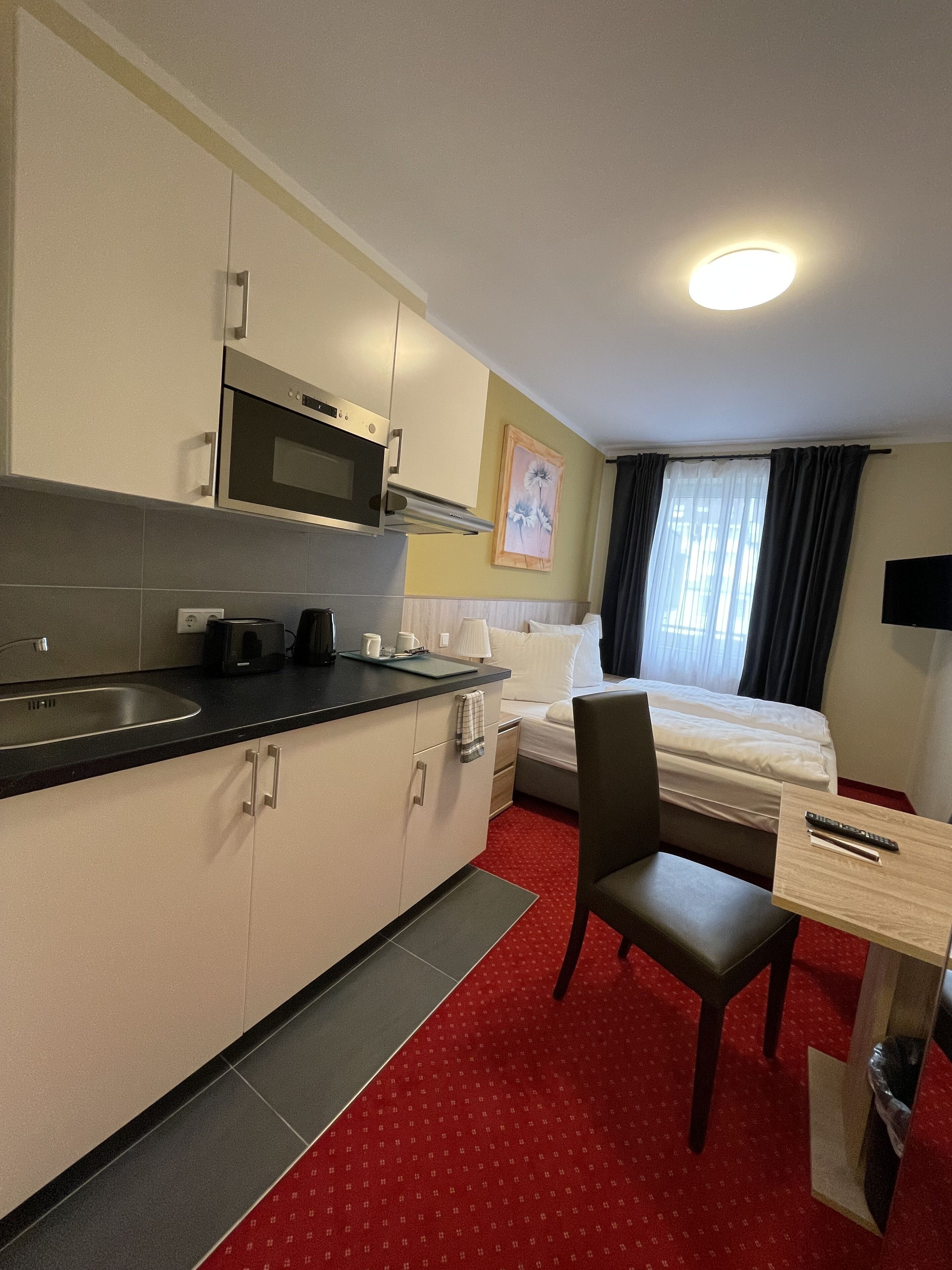 Een compacte hotelkamer met kitchenette, een bed, een klein bureau en een stoel.