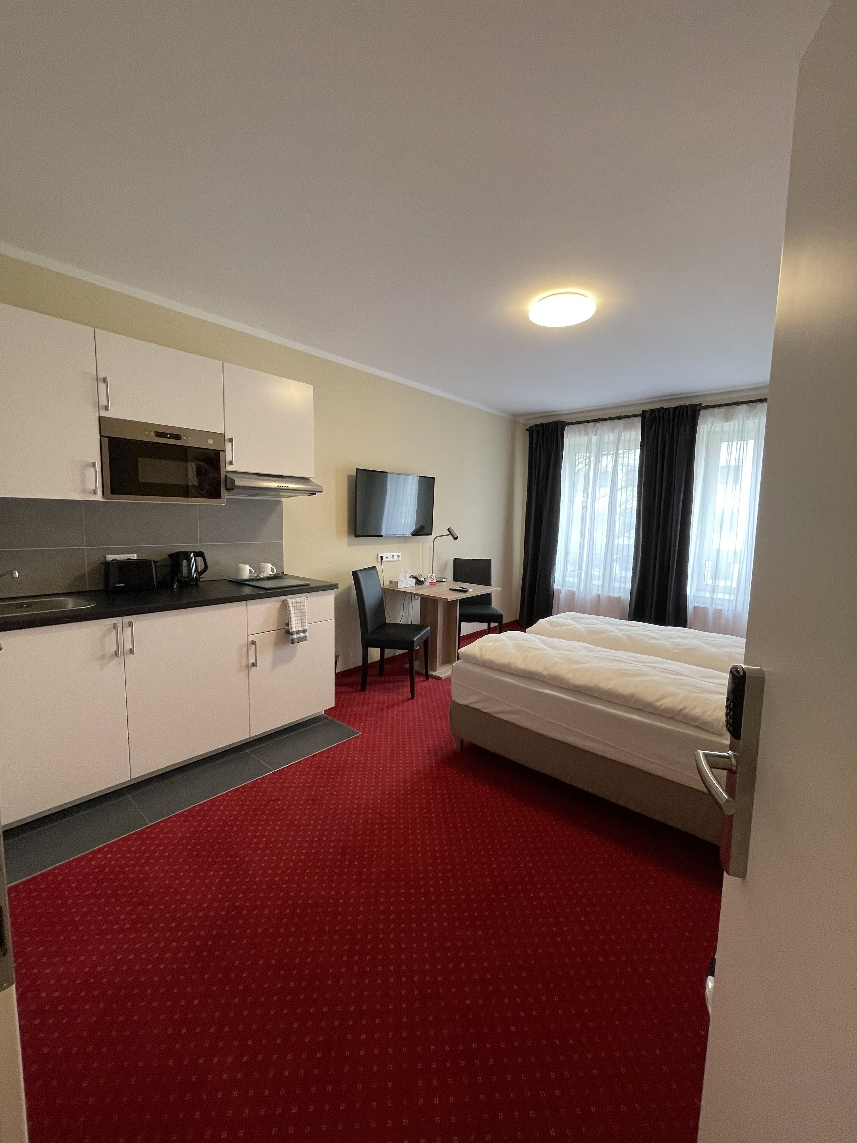 Hotelkamer met kitchenette, een bed, bureau met stoel en televisie.