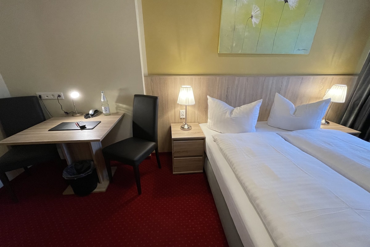 Une chambre d’hôtel comprenant un lit, un bureau, une chaise, une table de chevet et une lampe.