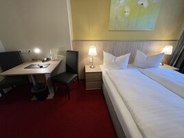 Una habitación de hotel con cama, escritorio, silla, mesita de noche y lámpara.
