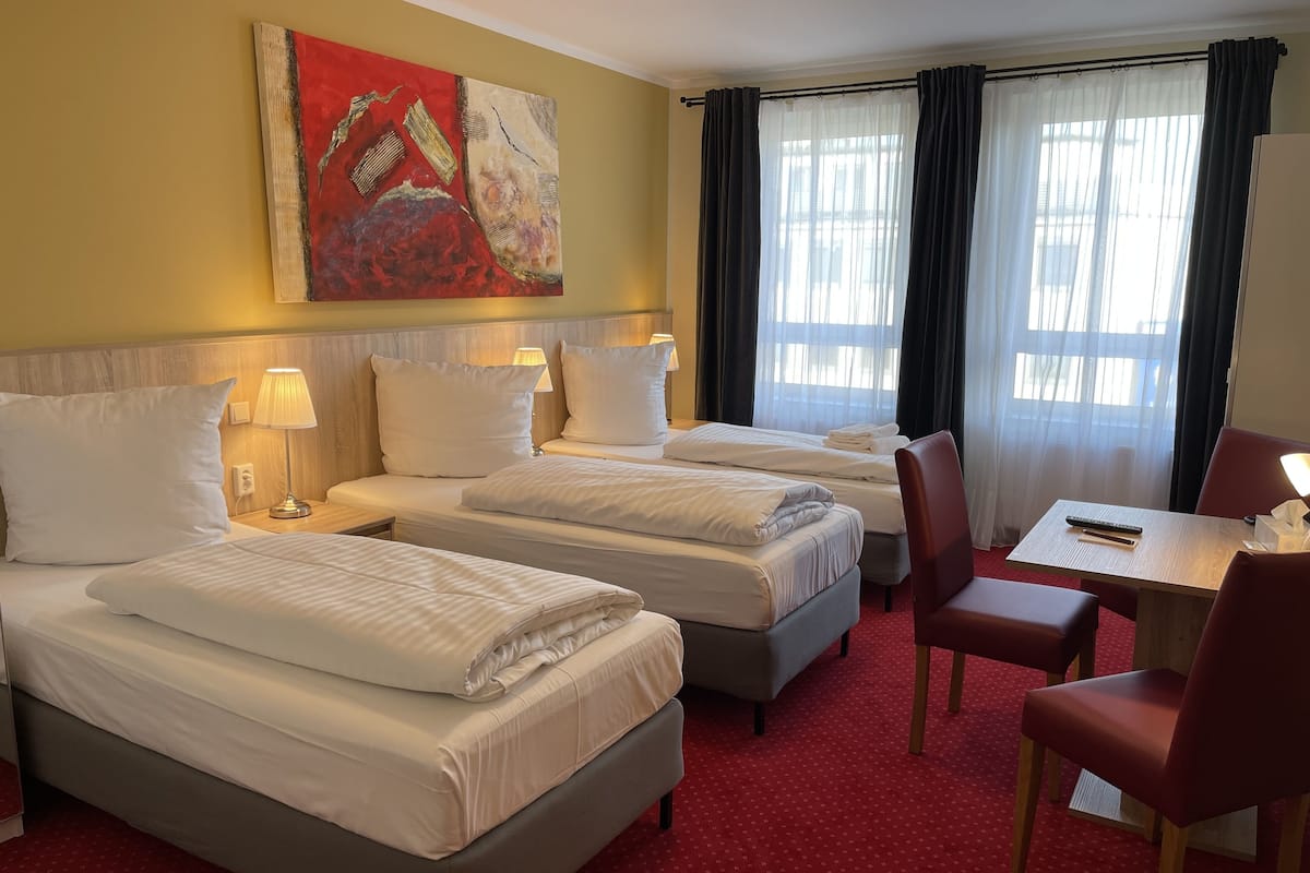 Une chambre d’hôtel avec deux lits, un bureau, une chaise et un tableau au mur.
